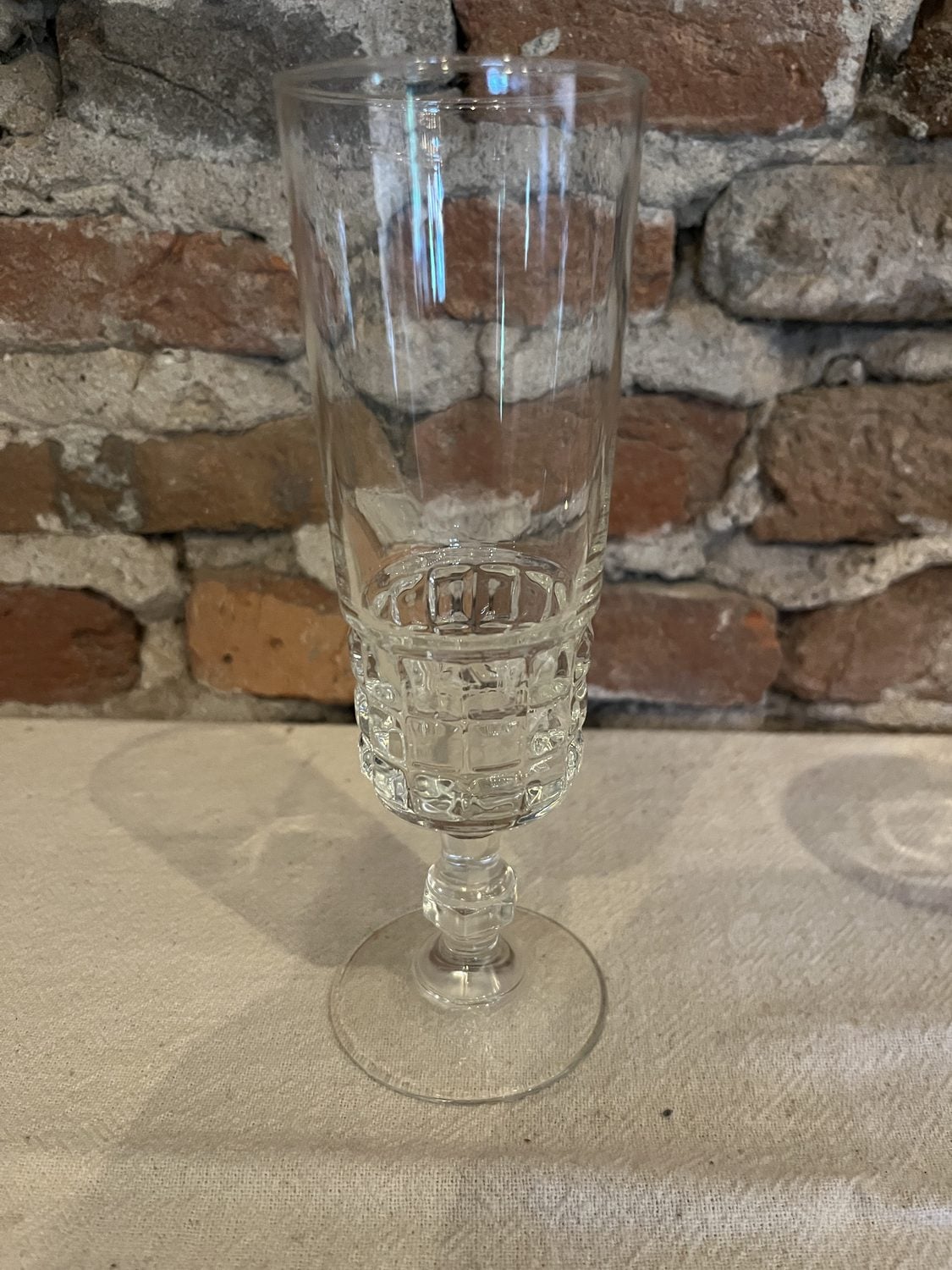 Hoog champagneglas op voet met een geslepen blokjesmotief, voor een bakstenen muur