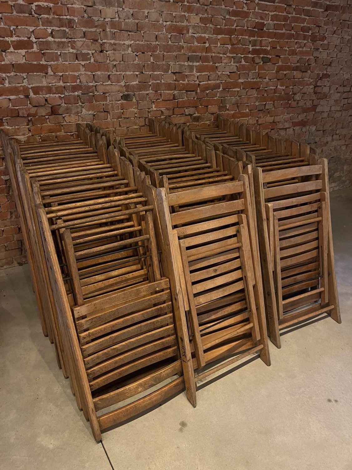 Stapels dichtgeklapte houten stoelen tegen een bakstenen muur in de schuur